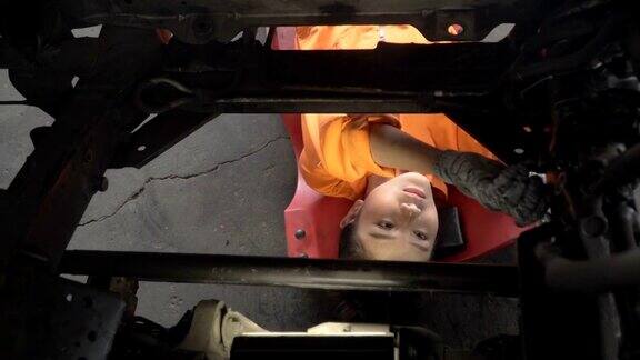 摄影车从正上方拍摄:亚洲年轻女性汽车技工试图从车辆引擎下面修理