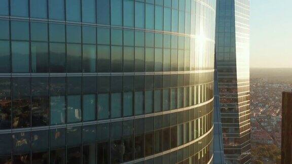上升的镜头沿着窗户和玻璃幕墙的办公大楼反映在城市的建筑和日落屋顶上挂着西班牙国旗