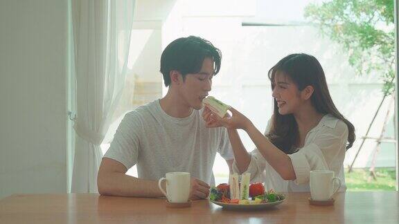 一对亚洲夫妇在家里厨房的桌子上给他的女朋友吃早餐三明治一对情侣的浪漫场景
