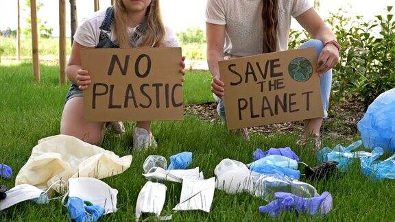 两个年轻女人蹲在一堆垃圾旁边上面贴着“拯救地球”和“禁止使用塑料”的海报在COVID-19大流行期间大量的垃圾被添加进来