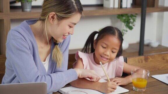 亚洲母亲一边教小女儿辅导家庭作业一边坐在家里用笔记本电脑学习母亲教女儿做作业儿童教育理念