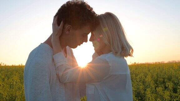 幸福的年轻夫妇亲吻在黄色的油菜花田在日落