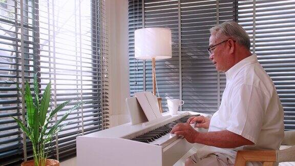 一位退休后的亚洲老人在自己家的客厅里练习弹钢琴