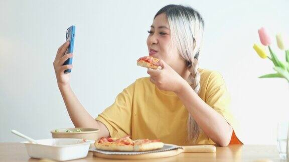 年轻的亚洲女子在家里吃披萨、沙拉和意大利面时用手机视频通话亚洲休闲餐饮