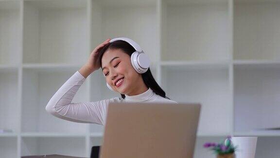 迷人的美丽的亚洲女人戴着耳机工作与笔记本电脑在家里享受听音乐