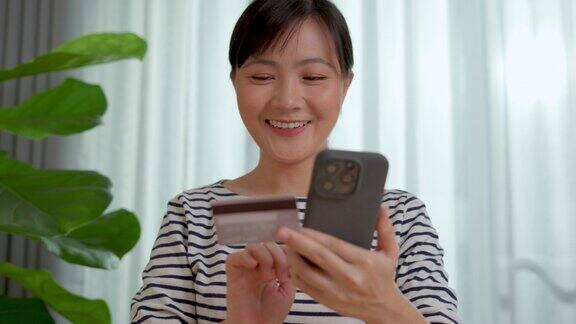 亚洲女性手持信用卡在家里用智能手机网购