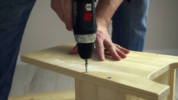 DIY家具组装工匠用电动螺丝刀将螺丝插入木板