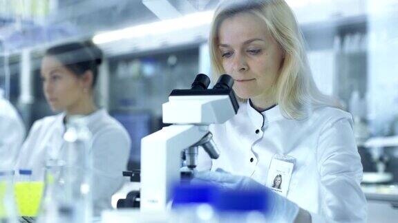 在显微镜下观察样品的女研究科学家们把滑片递给她的同事他们在一个大型研究中心实验室工作