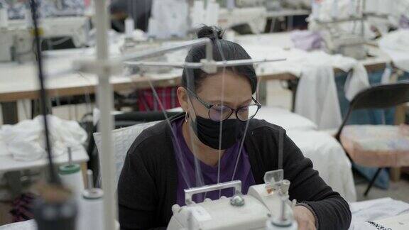 一名专注于缝制布料的妇女在一家服装厂的缝纫站穿着