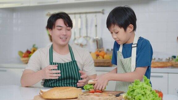 快乐的亚洲爸爸和可爱的小男孩在厨房做三明治当早餐家庭时间健康零食