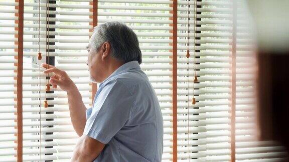 退休男子独自在家一个悲伤的老人独自站在窗前在想一些事情:悲伤和抑郁在一个自然的灯光镜头