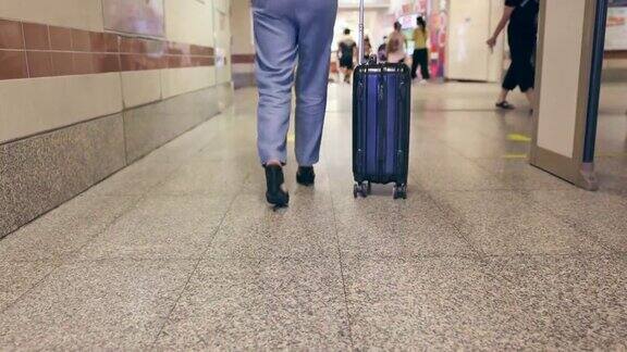 近景拍摄的是带着行李的女人的腿向机场候机楼走去背景是模糊的旅行人群