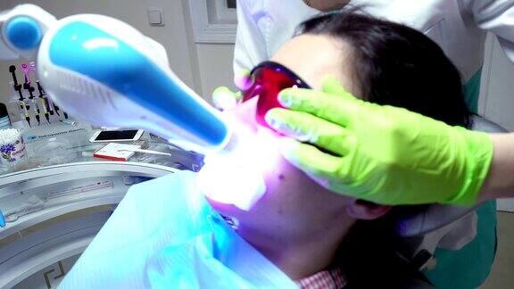 年轻女子嘴含扩张器戴着红色保护眼镜在牙科诊所进行紫外线美白