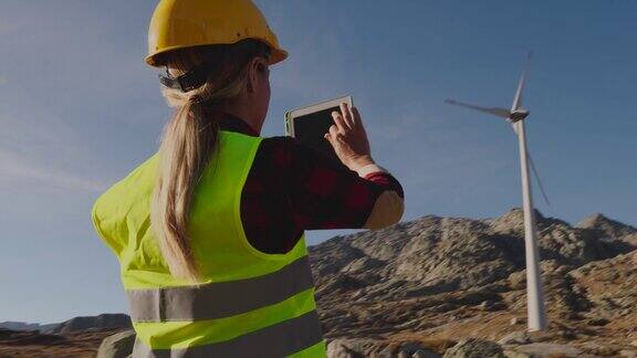 检查风力涡轮机的女工程师戴着安全帽使用着数码平板电脑