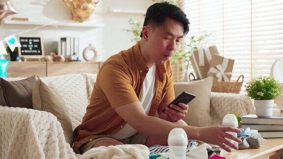 亚洲新爸爸丈夫男性用手检查清单上的物品准备婴儿出生时的婴儿用具在家里卧室里准备怀孕概念容器新爸爸用智能手机检查家里出生的婴儿的物品