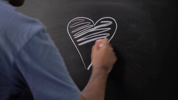 靠近男性用粉笔在黑板上画心形图标