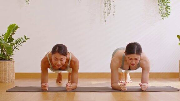 一对亚洲年轻女子坐在瑜伽垫上做呼吸练习瑜伽平板支撑式伸展强壮的肩膀在一起两位健康女性平衡身体的瑜伽冥想在舒适的家中放松