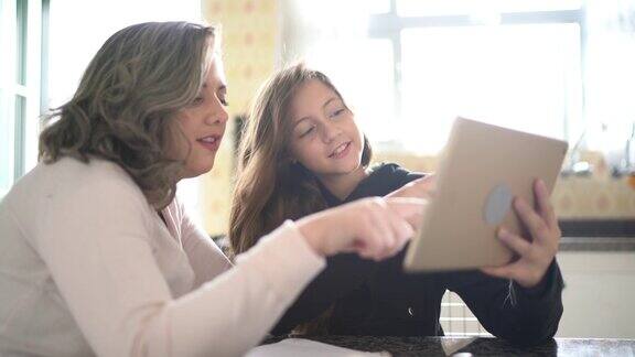 妈妈在家里帮助女儿做作业用平板电脑和视频聊天