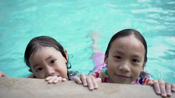 两个亚洲小女孩在游泳池里玩看着镜头微笑手持拍摄和真实生活