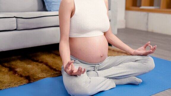 一位怀孕的亚洲妇女坐在自家客厅地毯上的瑜伽垫上放松她看都没看自己日渐隆起的肚子