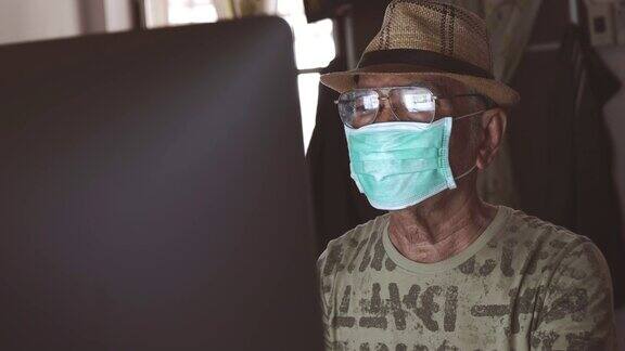 亚洲老年男性戴口罩保护新冠病毒或新冠病毒的场景是在冠状病毒大流行封锁期间在家使用电脑在家工作