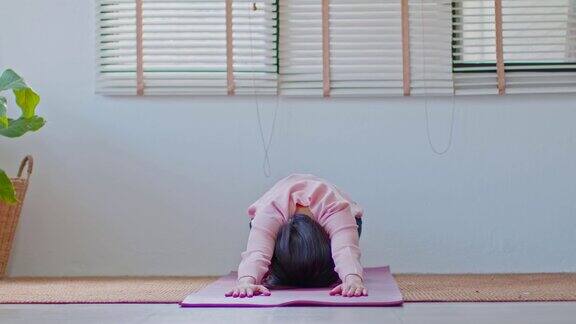 亚洲妇女在休闲做瑜伽锻炼瑜伽儿童姿势或Balasana平静的健康年轻女性呼吸和冥想与瑜伽在家里锻炼为健康的生活