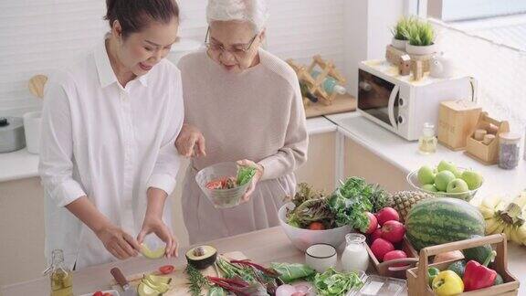 亚洲资深妈妈一边和中间的女儿在厨房准备健康的早餐蔬菜和水果一边选择她可以吃的蔬菜一起享受周末的活动高角度的正面视图