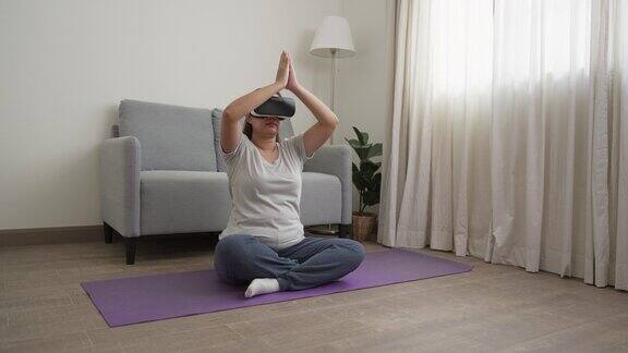 一位戴着虚拟现实眼镜的亚洲女性坐在家里的垫子上做瑜伽