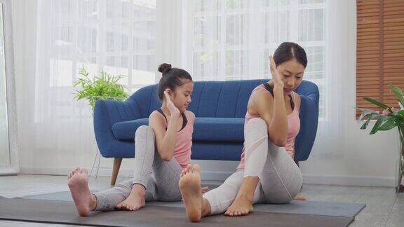 母亲正在教她的女儿如何做瑜伽姿势在家里做坐姿脊柱扭转式