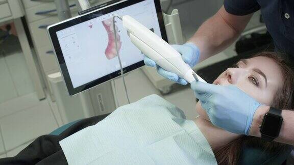 医生在诊所里扫描病人的牙齿牙医手里拿着一个手动3D扫描仪用来扫描下巴和嘴巴牙齿健康在医疗监视器上创建牙齿和牙龈的3D模型