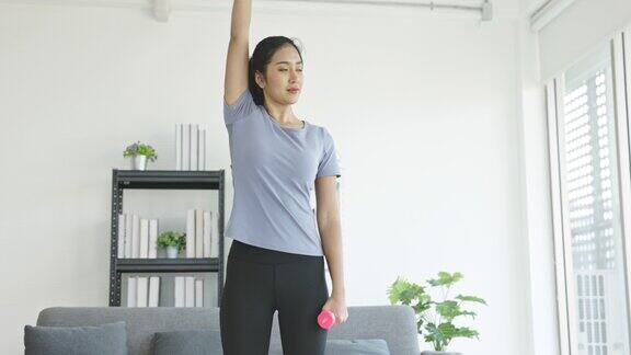 亚洲少女在家里的客厅里举着哑铃做有氧运动燃烧卡路里的运动塑造强壮的体型概念保健