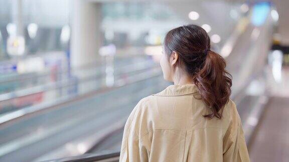 年轻的亚洲女乘客在机场候机楼或现代火车站亚洲女性通勤者带着行李乘坐自动扶梯