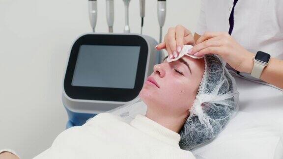 美容院美容师在为客户进行专业美容手术前用餐巾清洁面部皮肤护肤美容水疗概念