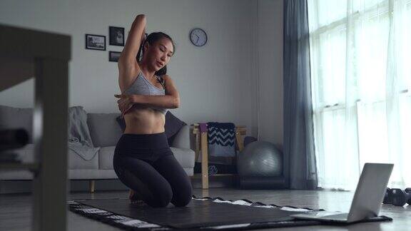 年轻的亚洲女性穿着运动服在家里锻炼在网上观看健身视频或在线健身课程使用笔记本电脑