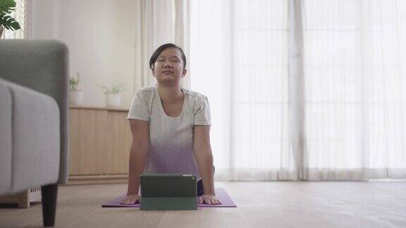 女人在家客厅练习瑜伽在平板电脑上观看在线教程