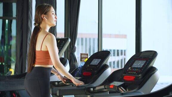 亚洲美女年轻的运动女性在跑步机上跑步喝矿泉水在健身房的智能手表上查看运动数据