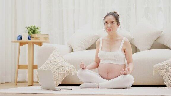 孕妇在客厅坐莲花位练习瑜伽冥想大肚子的亚洲妈妈在家里放松