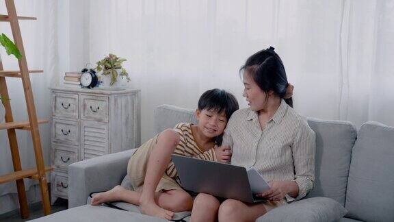 一个英俊的亚洲男孩跑到他的母亲身边坐下而他的母亲正在用笔记本电脑他的母亲深情地看着他轻轻地抚摸着儿子的头