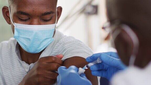 非裔美国资深男医生戴口罩在家为男性患者接种covid-19疫苗