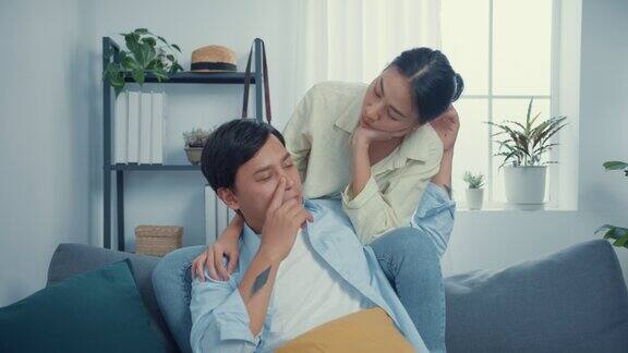 年轻的亚洲夫妇随意地坐在沙发上粘在一起拥抱甜蜜的时刻看着镜头在家里的客厅