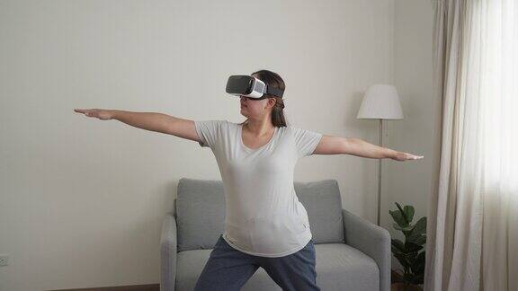 年轻的亚洲女子戴着虚拟现实眼镜站在家里练习瑜伽