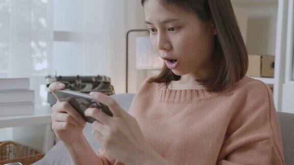 这是一名兴奋的年轻亚洲女子在家中客厅用智能手机玩游戏的照片
