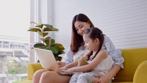 女儿和母亲坐在公寓的客厅里从笔记本电脑上在线学习微笑和快乐幼儿喜欢家庭写作活动照顾幼儿学习家庭生活方式