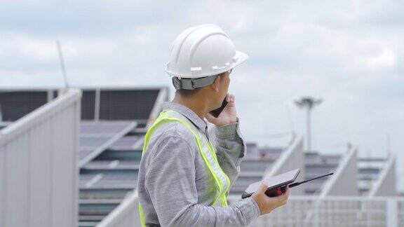 电气工程师在屋顶上检查太阳能电池板的构造并使用智能手机和数码平板电脑