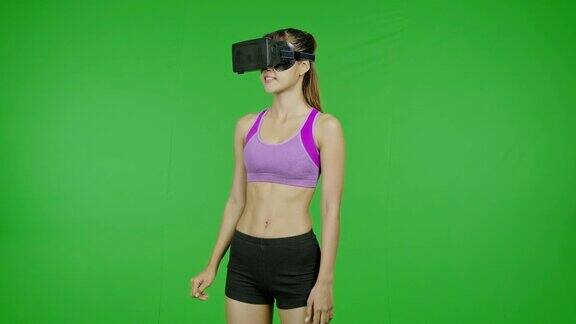 健康女性在绿色屏幕上的VR头盔中环顾四周点头微笑色度键技术增强现实亚洲妇女用于图形覆盖和剪切的目的