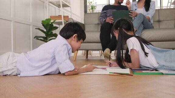亚洲的兄弟姐妹们一起用彩色铅笔画画父母们在沙发上悠闲地玩耍