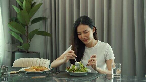 亚洲年轻女子微笑着舀起一盘沙拉在家里快乐地吃着