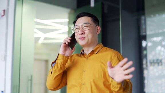 微笑的亚洲商人站在现代化的办公室里讲着智能手机