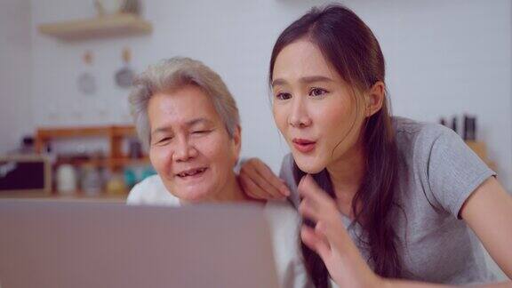 年轻的亚洲人和年长的女人在家里的厨房里使用笔记本电脑