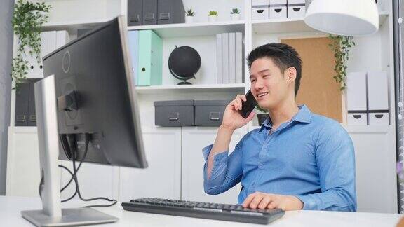 亚洲英俊的商人在办公室打电话和工作有吸引力的年轻男性员工坐在桌子上在工作场所用笔记本电脑打字用智能手机和同事讨论问题